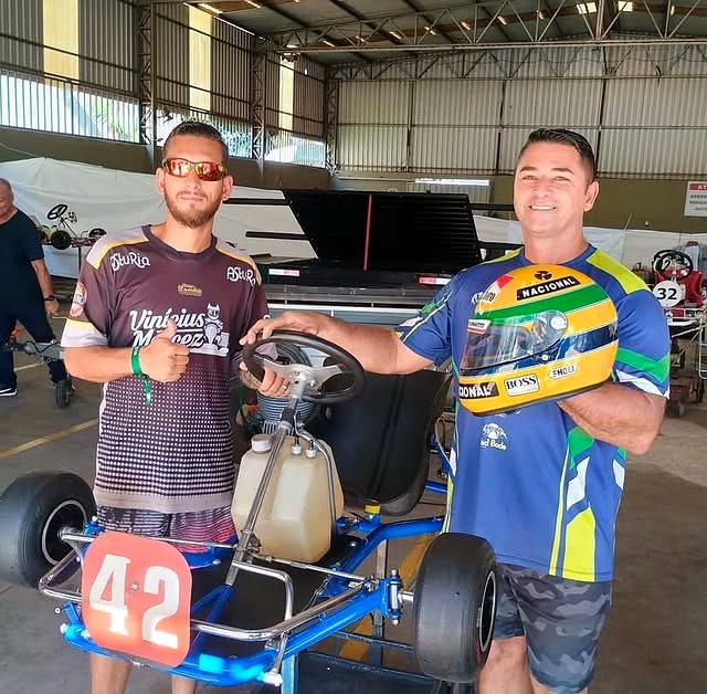 Zé do Bode e um piloto ao lado de um kart montado, dentro do galpão da equipe