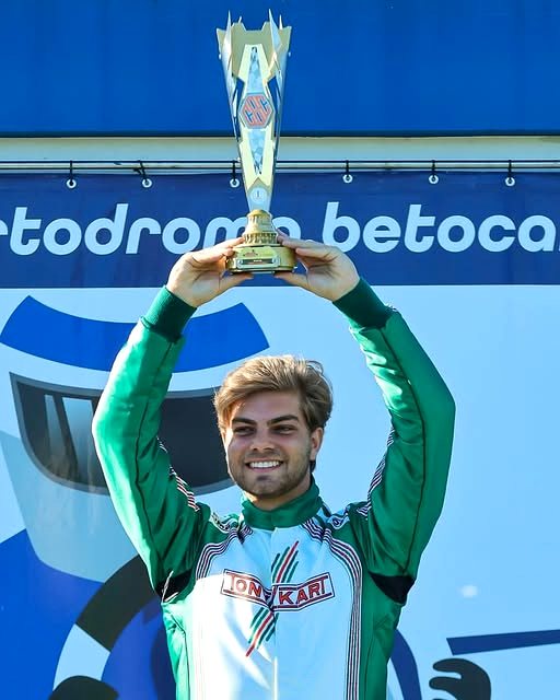Piloto de macacão erguendo um troféu da CBA no pódio do Kartódromo Beto Carrero